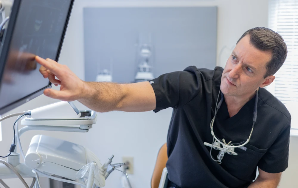 Dr. Lee Allen pointing at screen explaining dental implants treatment plan to patient at Creedmoor Road