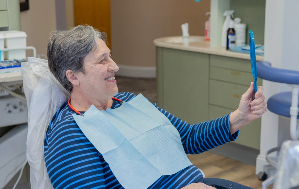 Happy patient checking smile in mirror after same day dental crown treatment at Creedmoor Road
