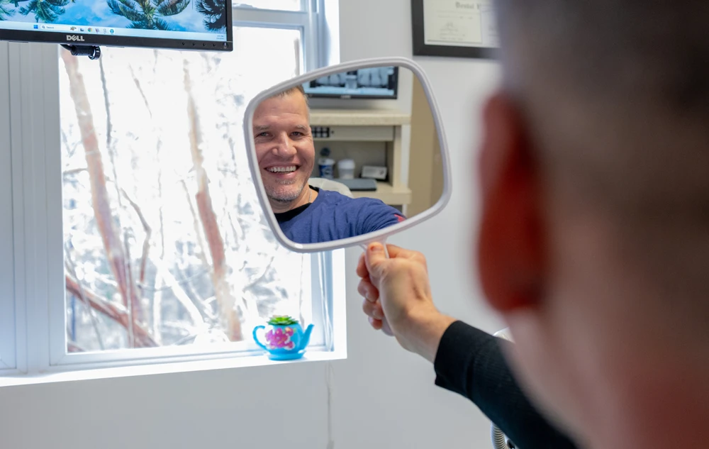 happy patient checking smile in mirror after treatment in creedmoor road dental office